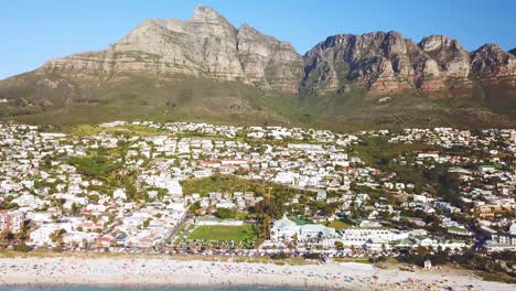 Luftbewegung-Entlang-Der-Reichen-Küste-Und-Eleganten-Häusern-Von-Camps-Bay-Kapstadt-Südafrika-Mit-Zwölf-Apostelbergen-Hintergrund