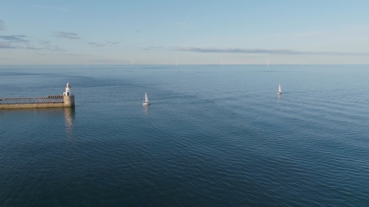 Two sailboats on calm sea near lighthouse in Northumberland, England
