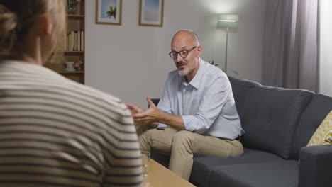 mature man sitting on sofa talking with female counsellor about general or mental health issue 17