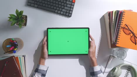 top down view of a laptop computer with mock up green screen chromakey display on a wooden office desk next to notebook with pens, glasses, and a glass of water. slow zoom out, close up