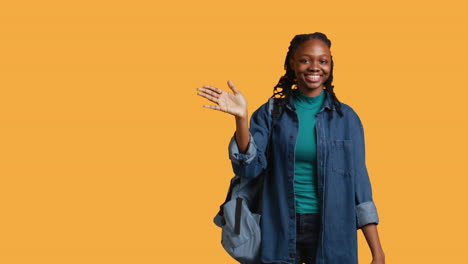 cheerful student witch school rucksack doing greeting hand gesture