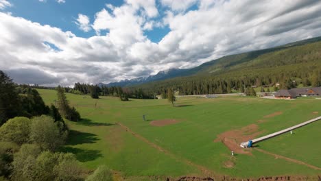 Aerial flight above forest and meadows near mountain horizon