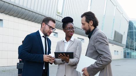 african american young businesswoman and two caucasian businessmen reading something on the tablet and talking in the street