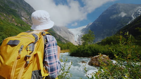 A-Tourist-With-A-Yellow-Backpack-Looks-At-A-Beautiful-Glacier-At-The-Top-Of-The-Mountain-Briksdal-Gl
