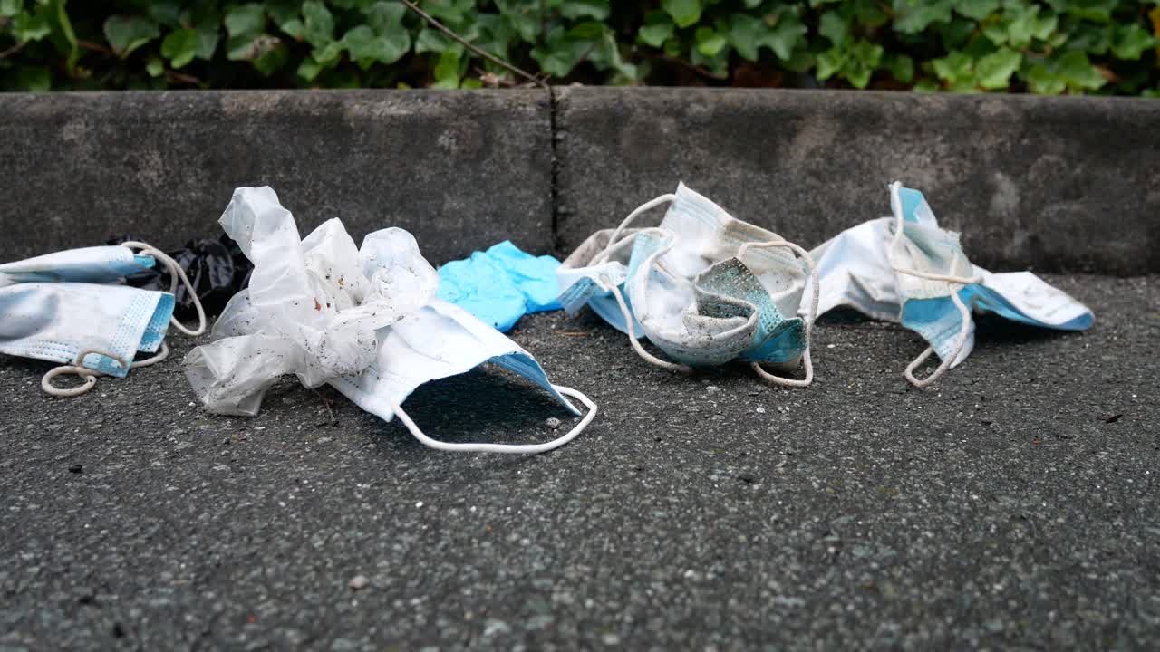 거리 보도에서 바람에 쓰레기를 불고 있는 더럽고 버려진 코로나 바이러스 마스크는 복사 공간 돌리 오른쪽을 닫습니다.
