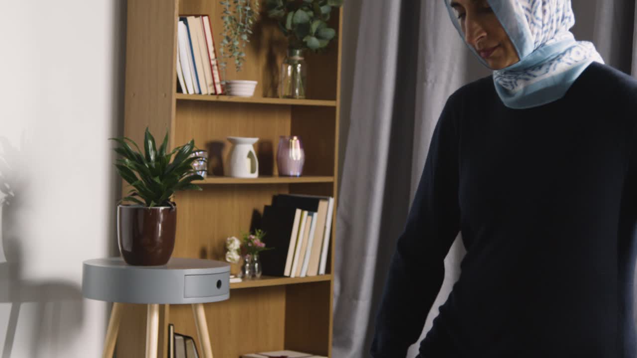 집에서 히잡을 쓰고 기도 매트에 무릎을 꿇고 기도하는 이슬람 여성