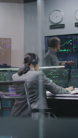 female financial analyst and investment manager discuss real-time stocks data on computer. colleagues work in bank office. big digital screens showing exchange market charts. vertical shot