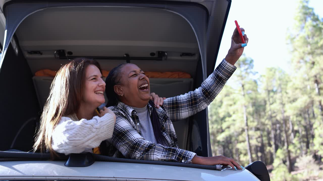 mujeres multirraciales mayores que usan un teléfono móvil para tomar una selfie dentro del techo de la camioneta