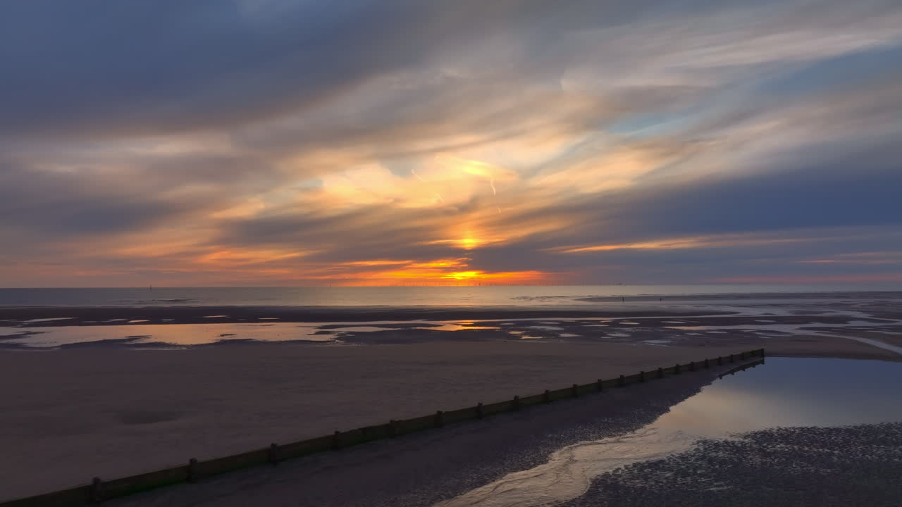 Flying over sands and past breakwater towards calm sea and setting sun. Fleetwood, Lancashire, UK