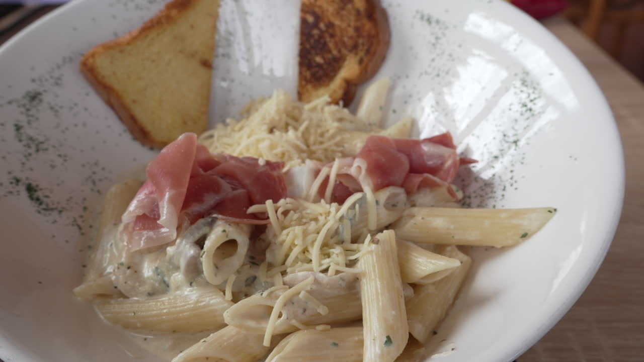 Una ciotola di fettuccine con formaggio grattugiato, pezzetti di prosciutto ed erbe fresche.