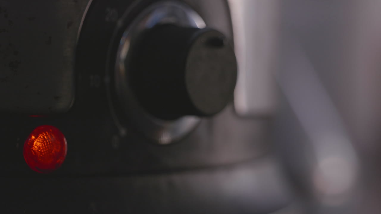 Close-up of a dark-colored appliance with a knob and a red indicator light