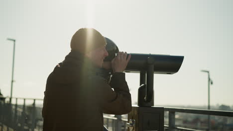 a father holds his son up to look through a telescope, the son peers through it while the father smiles, with warm sunlight reflecting on them