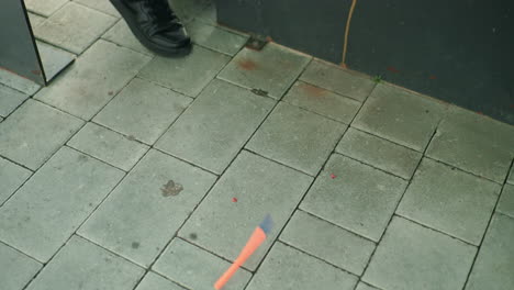 close up view of pen falling to ground near person in black shoe on outdoor tiled pavement, capturing moment of frustration or accident with focus on object in motion and urban environment