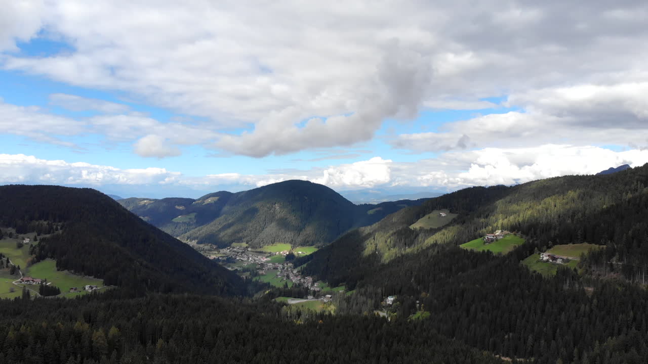 360 4K drone luftfoto af Dolomitterne i de italienske Alper på en overskyet dag med træer og byer beliggende i dale.