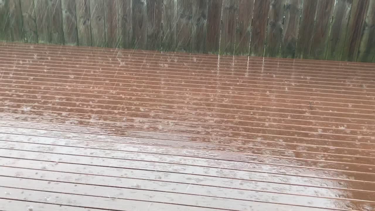Rain falling on rust stained deck against wooden fence during a winter day in Auckland New Zealand