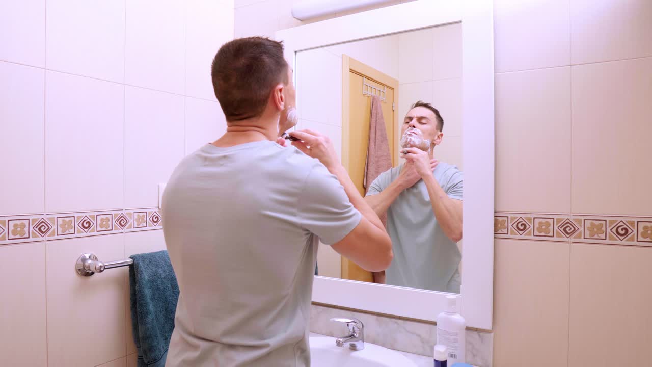Man shaving his beard in bathroom mirror