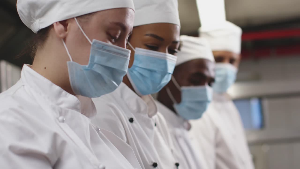 Diverse group of chefs wearing face masks standing in restaurant kitchen
