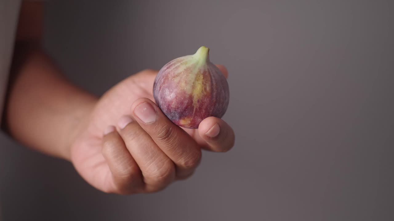 A hand holding a ripe fig fruit