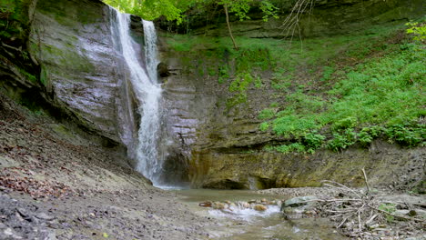 Slow-motion-zoom-in-of-floating-waterfall-down-mossy-cliff-wall-surrounded-by-green-idyllic-nature