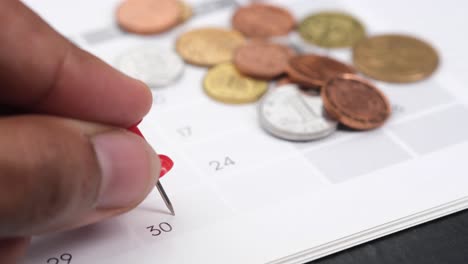 hand pinning a date on a calendar with coins