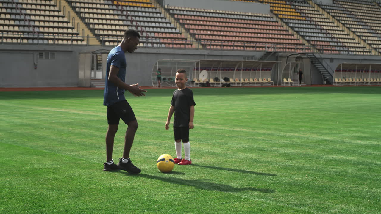 Black Coach Talking with Kid about Football on Stadium Pan around View of African American Trainer Showing Movements and Speaking with Mixed Race Boy during Football Workout on Stadium