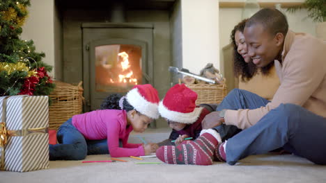 happy african american parents, son and daughter drawing at christmas in living room, slow motion
