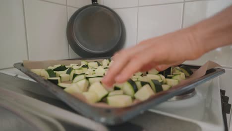 man placing chunks of zucchini evenly on a baking sheet