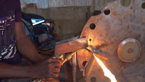 Primer-Plano-De-Las-Manos-De-Un-Trabajador-Africano-Soldando-Una-Sierra-De-Hierro-En-Su-Taller-De-Trabajo.