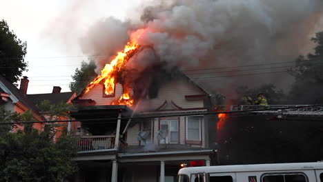 plumes of smoke rise from a raging house fire during the day