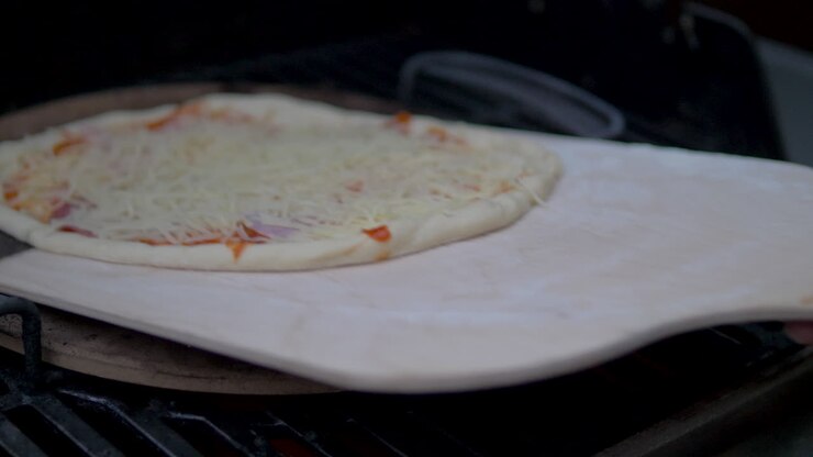 Putting a homemade delicious pizza into a wood fired grill with pizza stone