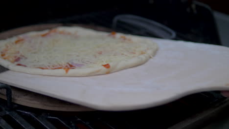 putting a homemade delicious pizza into a wood fired grill with pizza stone