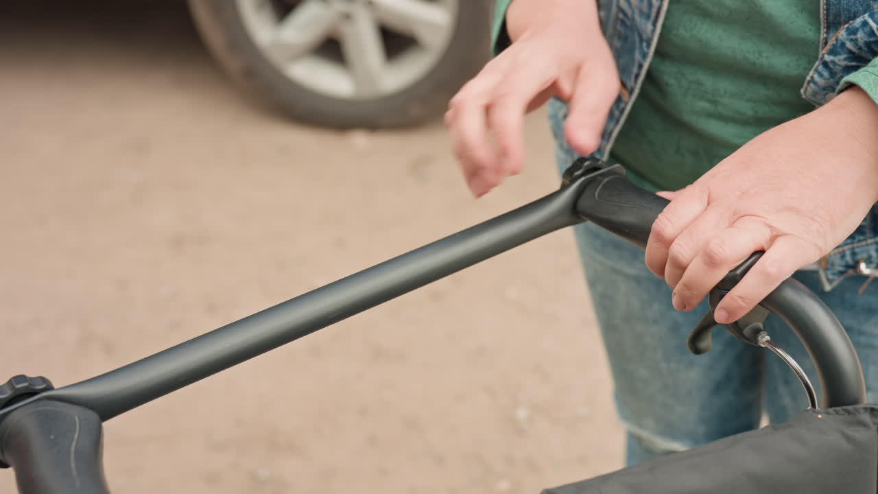 CloseUp Of Caregiver Detaching And Adjusting Push Handle On Wheelchair, Pushbar Release And Grip Detail, Denim Sleeve Visible, Practical Maintenance And Ergonomic Adjustment In Outdoor Parking Scene