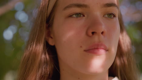 primer plano de una joven mirando atentamente con la luz del sol reflejándose suavemente en su cara, creando una expresión serena y enfocada, el fondo está hermosamente borroso con tonos verdes