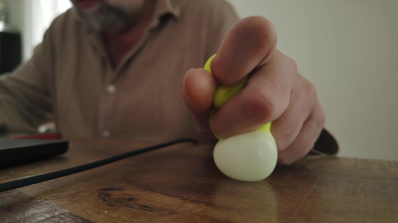 Man works on a laptop while squeezing a soft ball at home, evoking work pressure, stress relief, concentration and tactile coping.