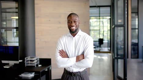 smiling african american businessman standing confidently with arms crossed in modern office