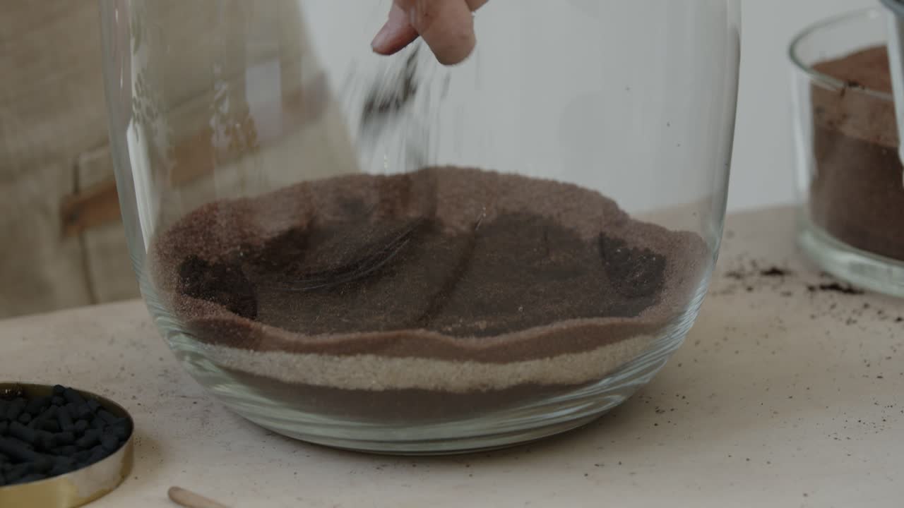 젊은 여성 식물학자는 유리 테라리움에 작은 생태계를 만들고 환경 보존 개념 클로즈업을 위해 거대한 항아리에 흙을 조심스럽게 넣습니다.