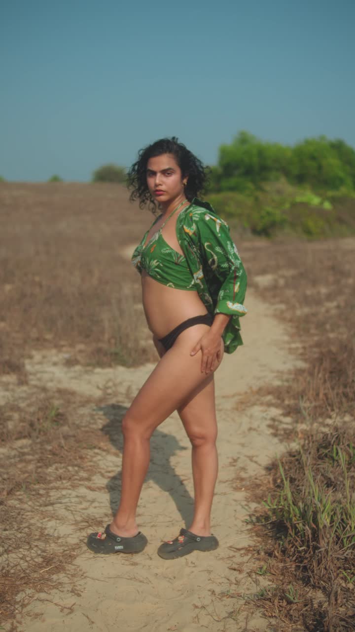 Donna sicura di sé che posa all'aperto su un sentiero asciutto con una maglietta verde e un bikini nero.