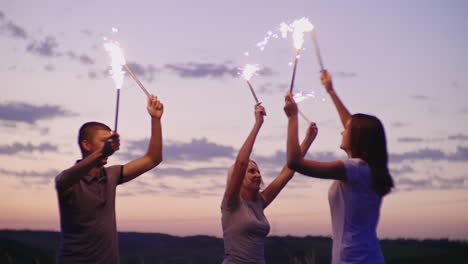 los amigos se divierten con fuegos artificiales después de la puesta de sol en una fiesta en la playa