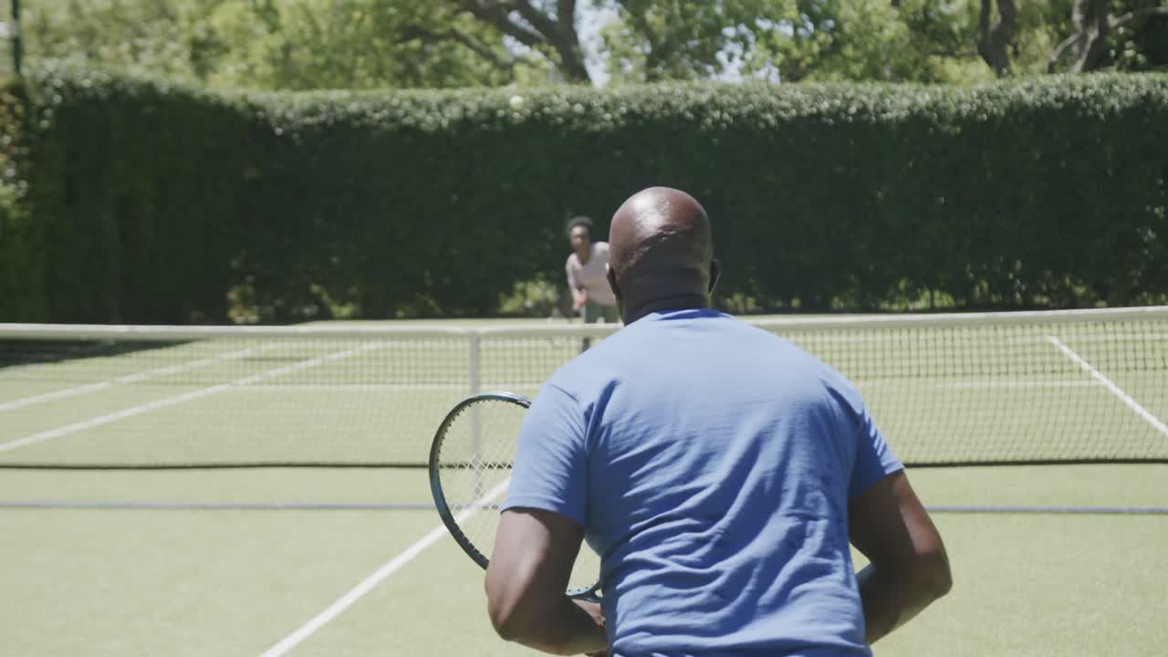 Happy senior african american couple playing tennis at tennis court in slow motion