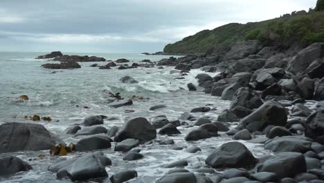 Slowmo---Wellen-Schlagen-An-Einem-Bewölkten-Tag-Auf-Felsen-Am-Strand-In-Bluff,-Neuseeland