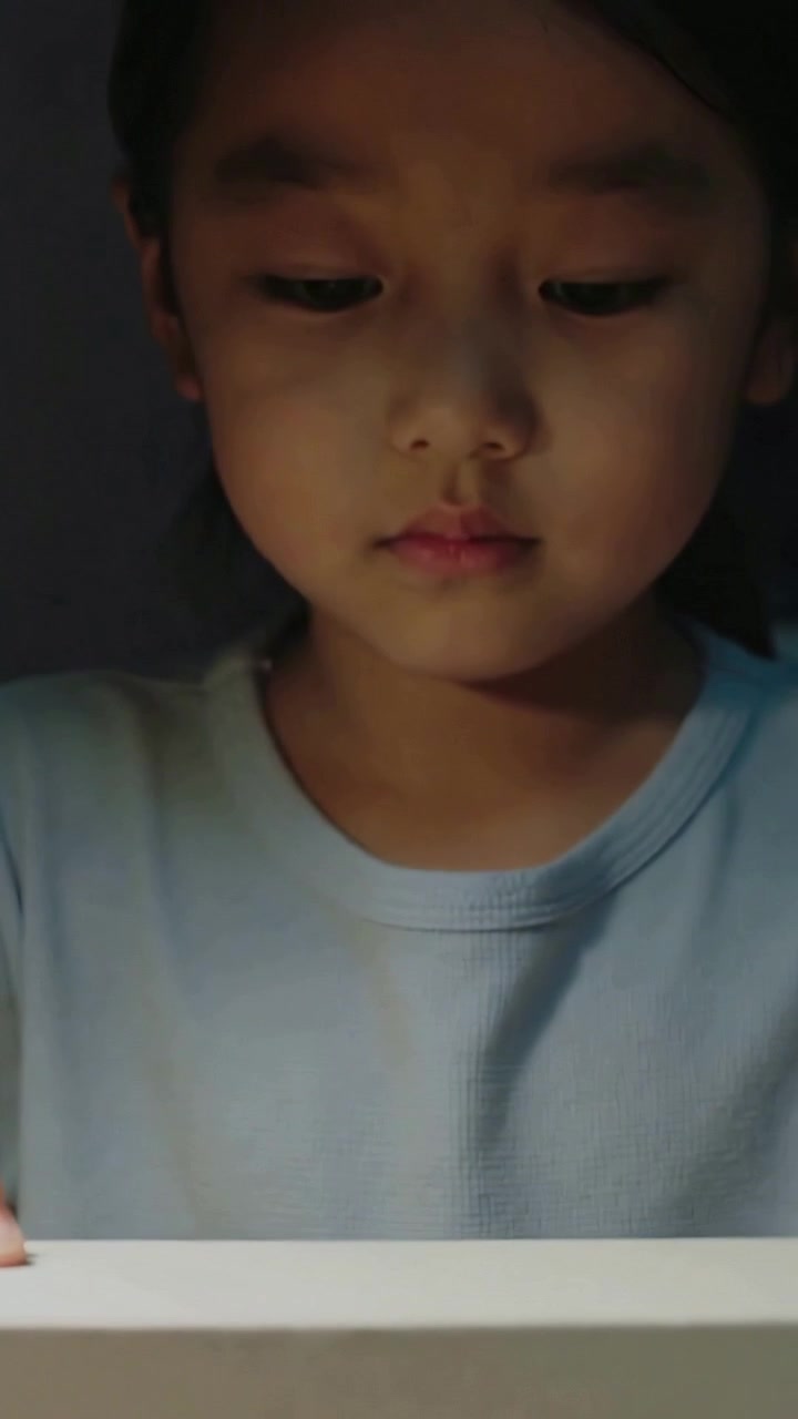 Video verticale: Spostando le mani del bambino che rivelano il viso al tavolo, mentre ispeziona una scatola rettangolare chiara