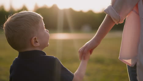 little boy holds mother hand walking together along meadow