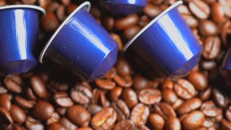 Coffee-capsules-in-focus-lying-on-roasted-coffee-beans-in-background