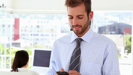 Man-texting-on-phone-while-colleague-works-behind-him