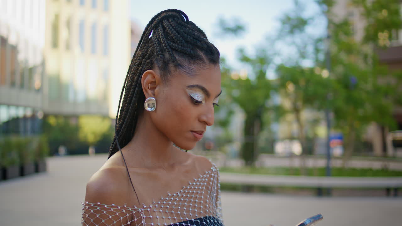 mujer de moda de primer plano mensajería teléfono móvil en la plaza de la noche. trenzas señora