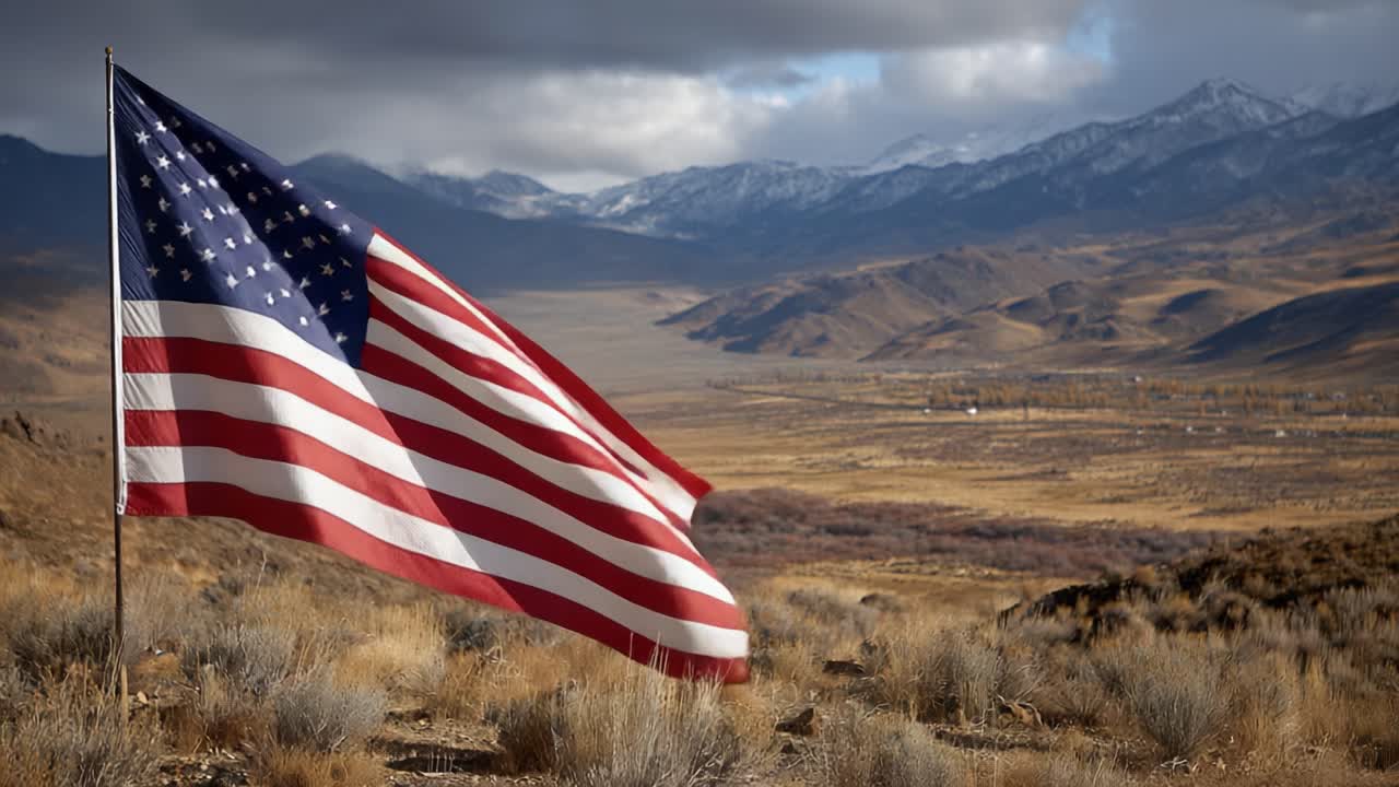 A Majestic American Flag Waves Gracefully in the Wind Against a Stunning Mountain Landscape Featuring Rocky Peaks and Vibrant Nature's Colors