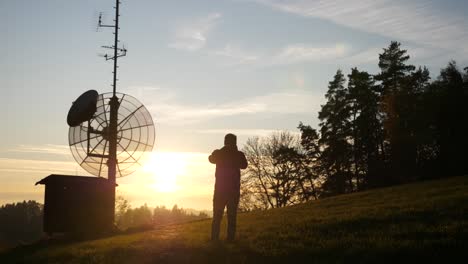 photographer is walking into the sunset and taking pictures behind a transmission mast