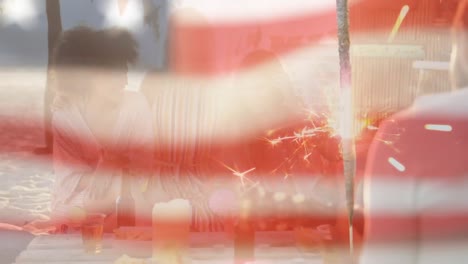 Animation-of-american-flag-waving-over-group-of-friends-having-party-on-beach