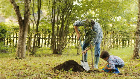 Portrait of a little boy and his dad planting a tree. Together they put the soil on the roots of the tree. Blurred background