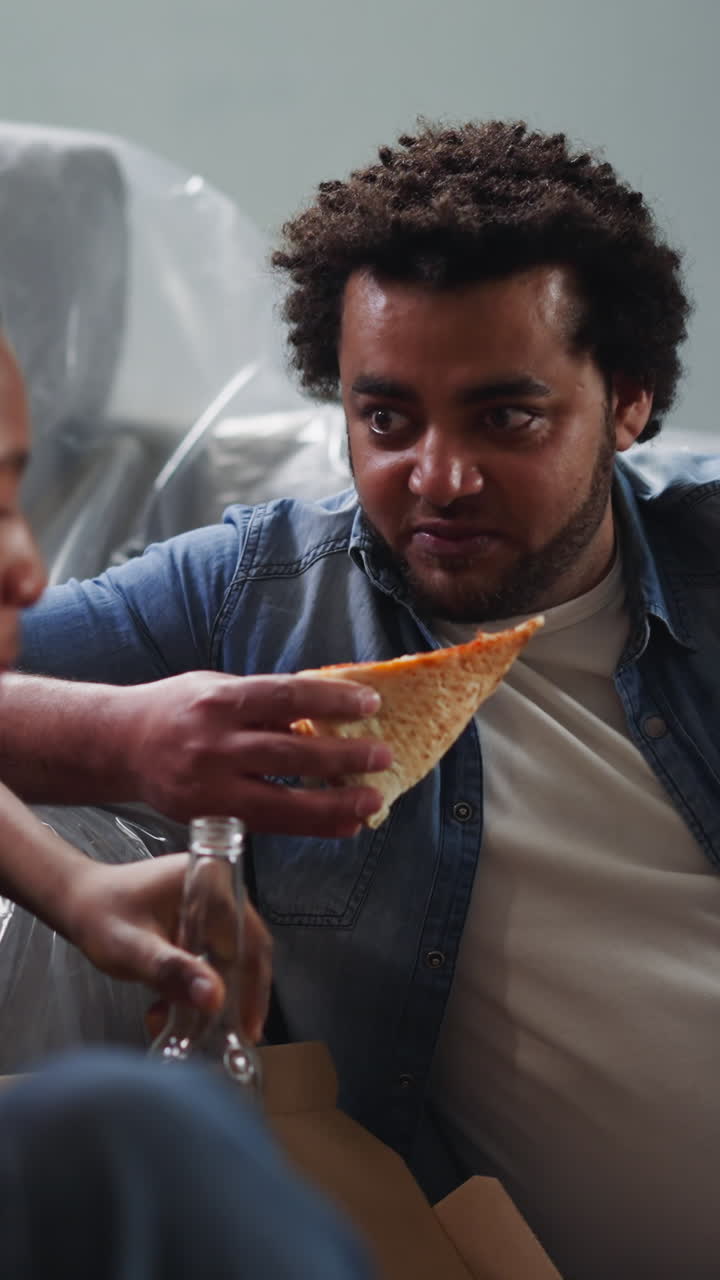 Positive guys enjoy beer and pizza on floor near sofa in renovated room closeup. Homeowners have little party after work. Rest and relax
